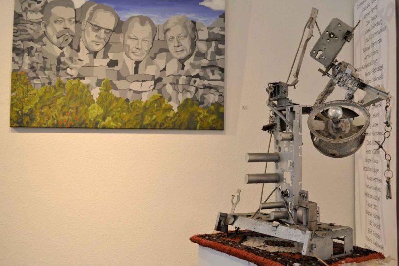 Vor der Acrylzeichnung „Genossenschaft“ schafft sich die Installation „Stubenlampe“ Raum.