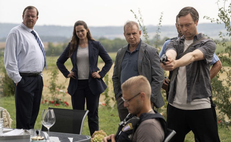 Stephan Ernst (re) stellt bei der Tatortbegehung den Tathergang für den Verfassungsschützer Vogel (Bernd Hölscher, li), Staatsanwältin Weber (Mi) und den Ermittler Bartels (Joachim Król,) nach.