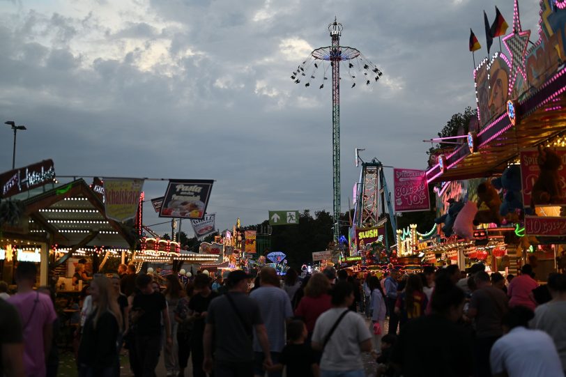 Besucher der abendlichen Cranger Kirmes mit Hochfahrbetrieb Bayern Tower Riesenrad Jupiter, Kettenkarussel Wellenflug Blick auf die Cranger Kirmes von der Rathausstraße aus. Im Bild Riesenrad Jupiter, Hochfahrbetrieb Evolution sowie der Turm vom Hochfahrbetrieb Hangover The Tower