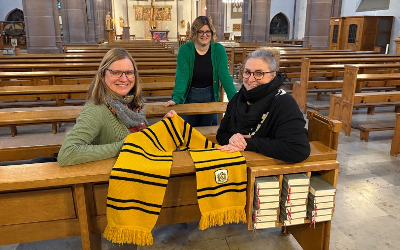 Der Hufflepuff-Schal liegt schon bereit: Die Organisatorinnen (v.li.) Melanie Jansen, Bettina Aust und Katja Lueg freuen sich auf den Harry Potter-Gottesdienst am Samstag, 28. Februar 2026, in der Herz-Jesu-Kirche in Herne-Süd.