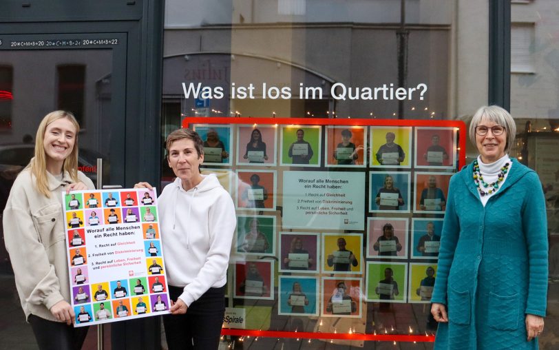 Die Caritas-Mitarbeiterinnen (v.li.) Lisa Köhler, Ulrike Lange und Mechthild Greifenberg präsentieren die Fotocollage „Für Menschenrechte“ vor dem Caritas-Quartiersbüro.