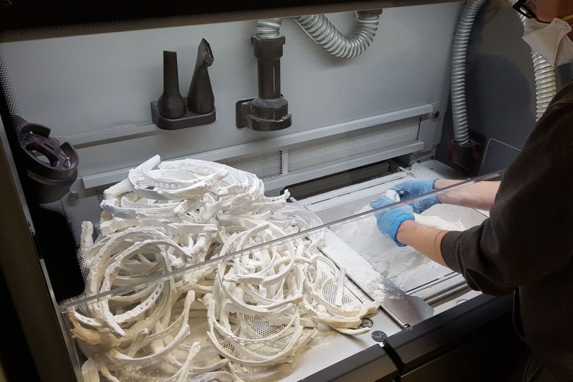 Ober- und Unterteile der Schutzmaske entstehen im 3D-Druckverfahren aus feinstem Kunststoffpulver, aus dem sie – wie hier im Bild – ausgegraben werden.