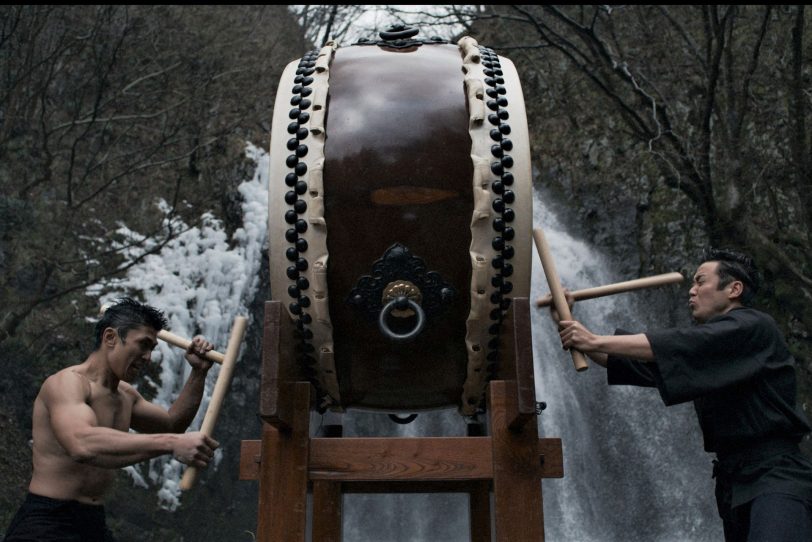 Die „dicke Trommel“ wird von zwei Musikern vor dem großem Wasserfall der Insel Sado geschlagen.