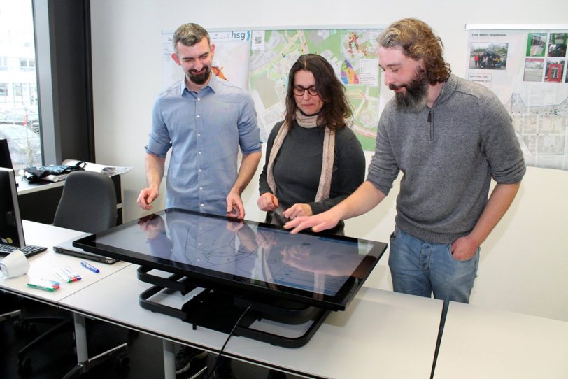 v.l. Dr. Raphael Sieber, Prof. Dr. Heike Köckler und Daniel Simon, Doktorand im DoCH, vor dem Maptable in der hsg Bochum.