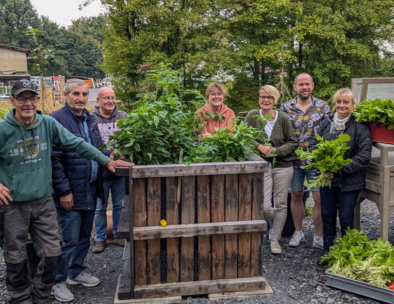 Das Caritas-Team mit André Blumig (2. v. r.), Claudia Krall (3. v. r.) und Gerlinde Bueren (4. v. r.) präsentiert gemeinsam mit „In- and Outdoor ü50“-Teilnehmenden einen Teil der Gemüseernte.
