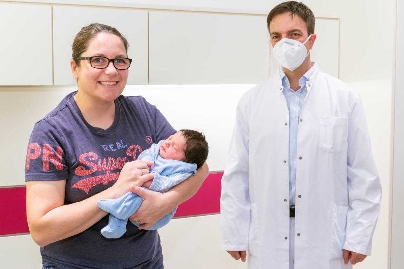 Jubiläumsbaby Nele auf dem Arm von Mutter Saskia, die ihre Frau bei der Entbindung begleitet hat, und Chefarzt Valentin Menke.