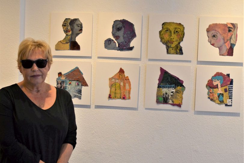 Annette Ihme-Krippner vor einer Kopf-Serie in Mischtechnik auf gerissener Filzpappe.