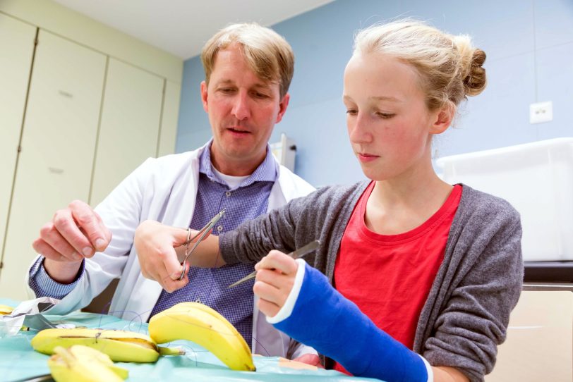 Dr. Micha Bahr, Leitender Oberarzt der Klinik für Kinderchirurgie mit einer Besucherin beim Bananen operieren