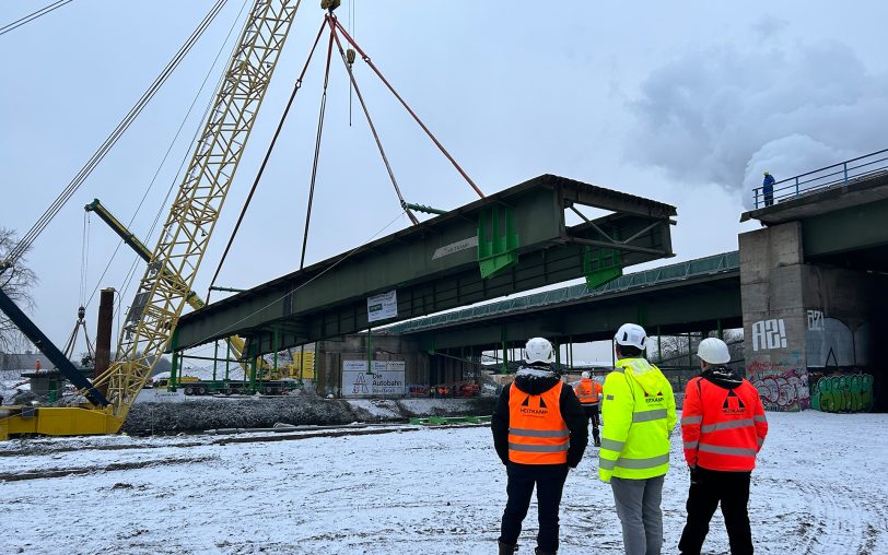 Die A43-Brücke über den Rhein-Herne-Kanal wurde am Mittwoch (17.1.2024) durchtrennt und mit Hilfe von zwei Spezialkränen an Land gehoben - hier ist das größere Brückenteil mit einem Restgewicht von rund 150 Tonnen im Bild, welches durch einen Schiffskran auf die verschneite Fläche im Vordergrund platziert wird.