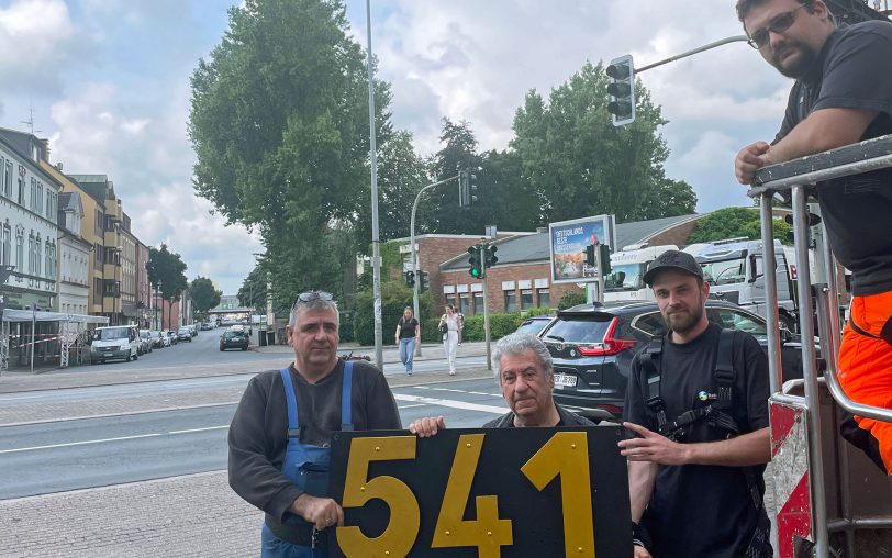 Vor der Montage: Constantin Costaras und sein Sohn Elias (li.) mit den Stadtgrün-Mitarbeitern Moritz Rörtgen und (im Steiger) Kevin Töpfer. Zehn Minuten später hing die neue Nummer am Cranger Tor.