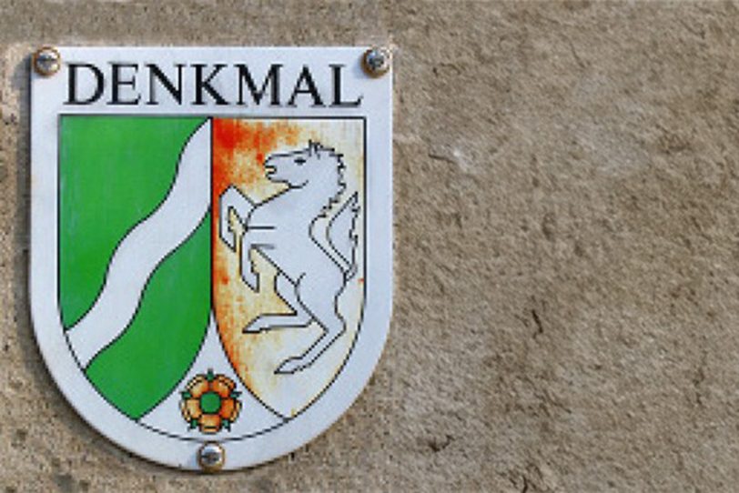 Emailschild mit dem Denkmalschutzzeichen befindet sich an alten, denkmalgeschützten Häusern.