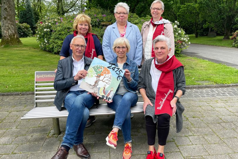 Der rote Schal signalisiert Gesprächsbereitschaft: Antje Grihn und Karin Moczarski (Mitte), aktiv in der Kreativgruppe des Fördervereins, übergaben auf dem Wiescherfriedhof einen symbolischen „Scheck“ über 2.415 Euro an den Fördervereinsvorsitzenden Pfarrer Frank Obenlüneschloß, Hospizdienst-Koordinatorin Karola Rehrmann (hinten re.) und die Zeitschenkerinnen Cordula Skrabaczewski (hinten li.) und Christa Schodl (vorn re.)