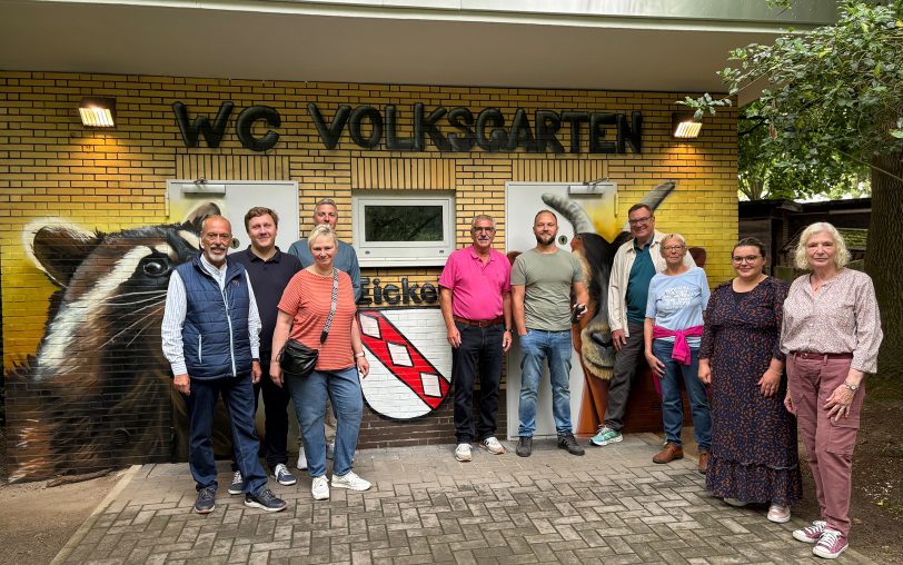 Bezirksbürgermeister Arnold Plickert (5.v.li.) und Graffiti-Künstler Patrick Sziedat (5.v.r.) sowie weitere Beteiligte vor der renovierten Toilettenanlage im Eickeler Volksgarten. David Hucklenbroich (Fachbereichsleiter Stadtgrün, 4.v.l.), Martina Schneider (zweite Vorsitzende Förderverein Mini-Zoo, 3.v.l.) und Ulrich Syberg (Wohnen in Herne, 4.v.r.) waren mit vor Ort.