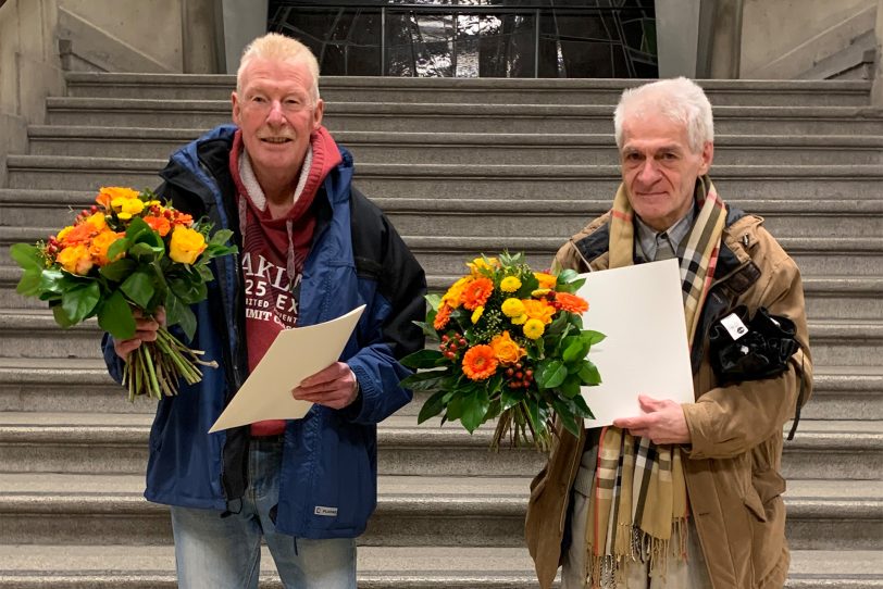 v.l. Die beiden Ehrenamtler des Zeppelin-Zentrums Detlef Oppelt und Peter Görgen mit Urkunde und Ehrennadel auf der Treppe zum Ratssaal.